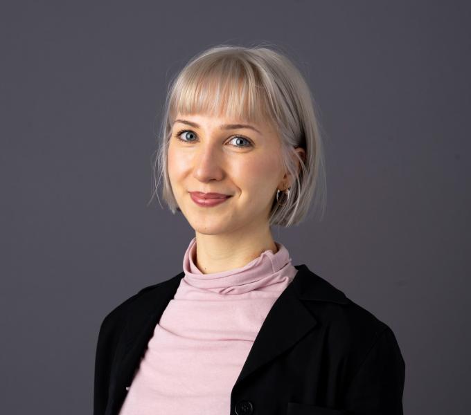 Headshot of a woman with short blonde hair, a pink top, and black blazer
