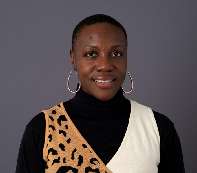 A woman with short hair and hoop earrings, wearing a black top and printed vest