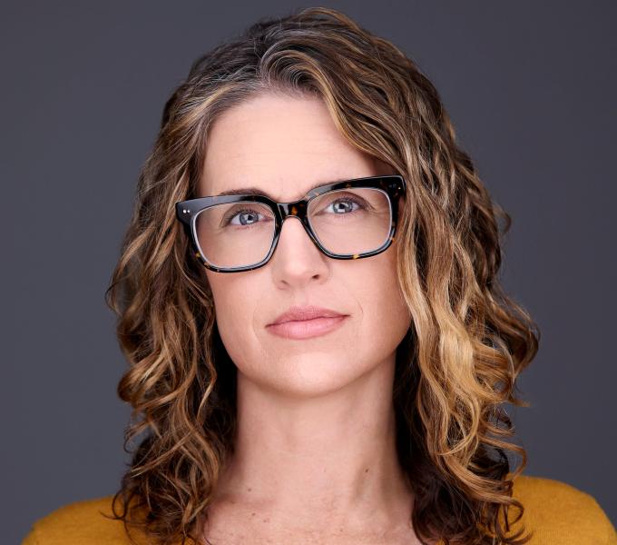 A woman with curly hair and dark glasses wearing a yellow top